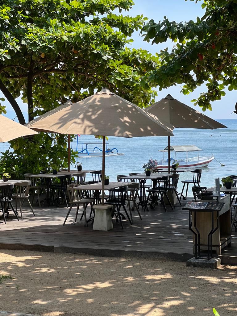 Open-air outdoor beachfront dining tables under shaded umbrellas